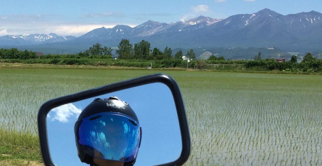 北海道の山々とサイドミラーに写るヘルメット